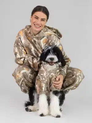 Woman and her dog wearing matching Comfrt CloudTouch Camo fleece hoodies and loungewear sitting together on the floor.