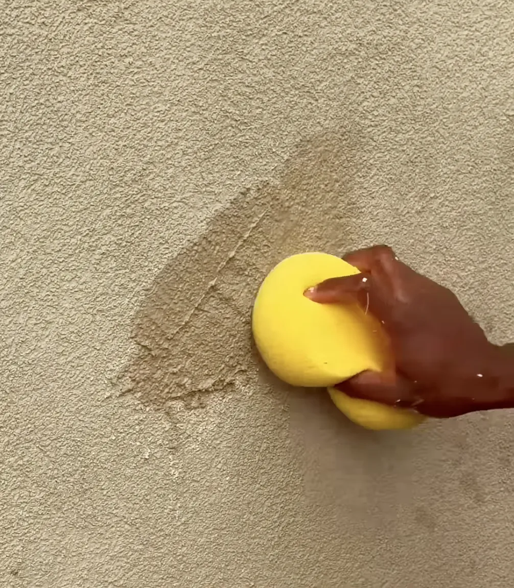 hand with a sponge smoothing over tan stucco on the wall