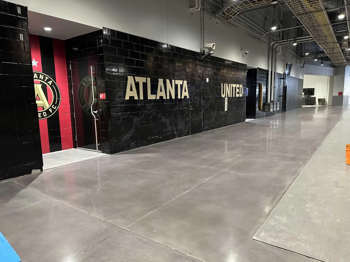 Bright, modern office lobby with a seamless, reflective epoxy floor in a soft aqua hue, surrounded by glass walls and contemporary furniture. The space feels inviting, clean, and showcases the practical benefits of epoxy flooring in commercial settings.