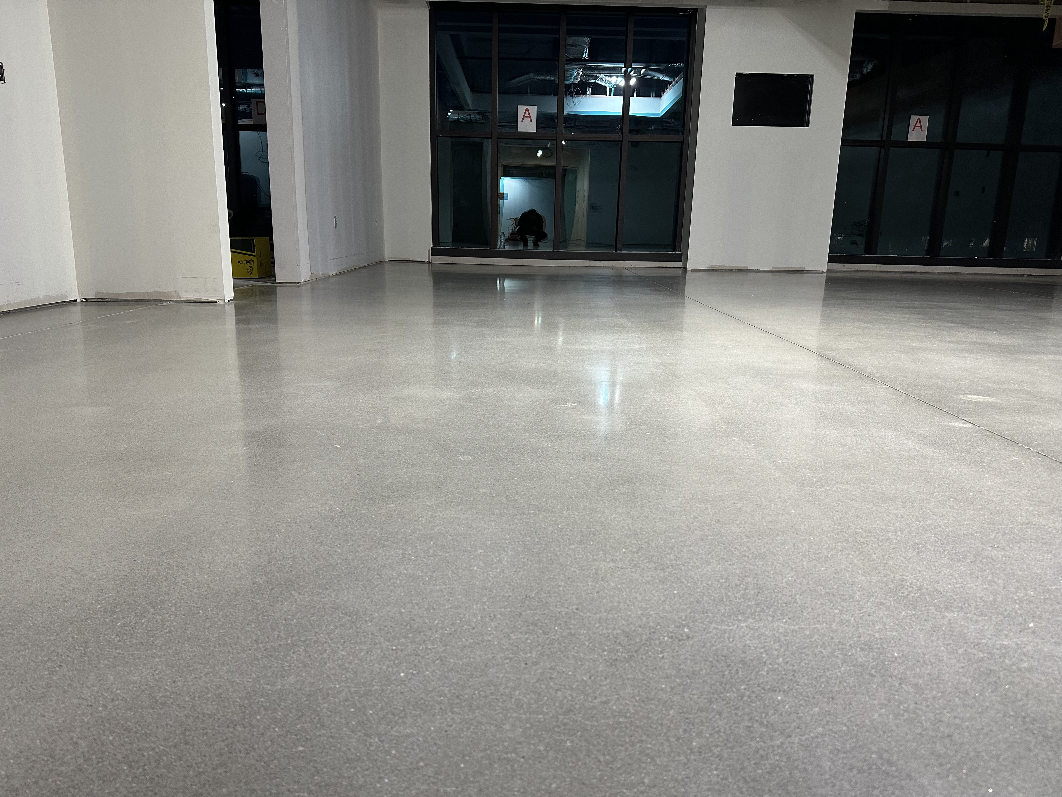 Modern living room with high-gloss, aqua-toned epoxy floor reflecting natural light, minimal furniture, and large windows. The space feels fresh, open, and professionally finished, highlighting the transformation possible with expert floor coating.