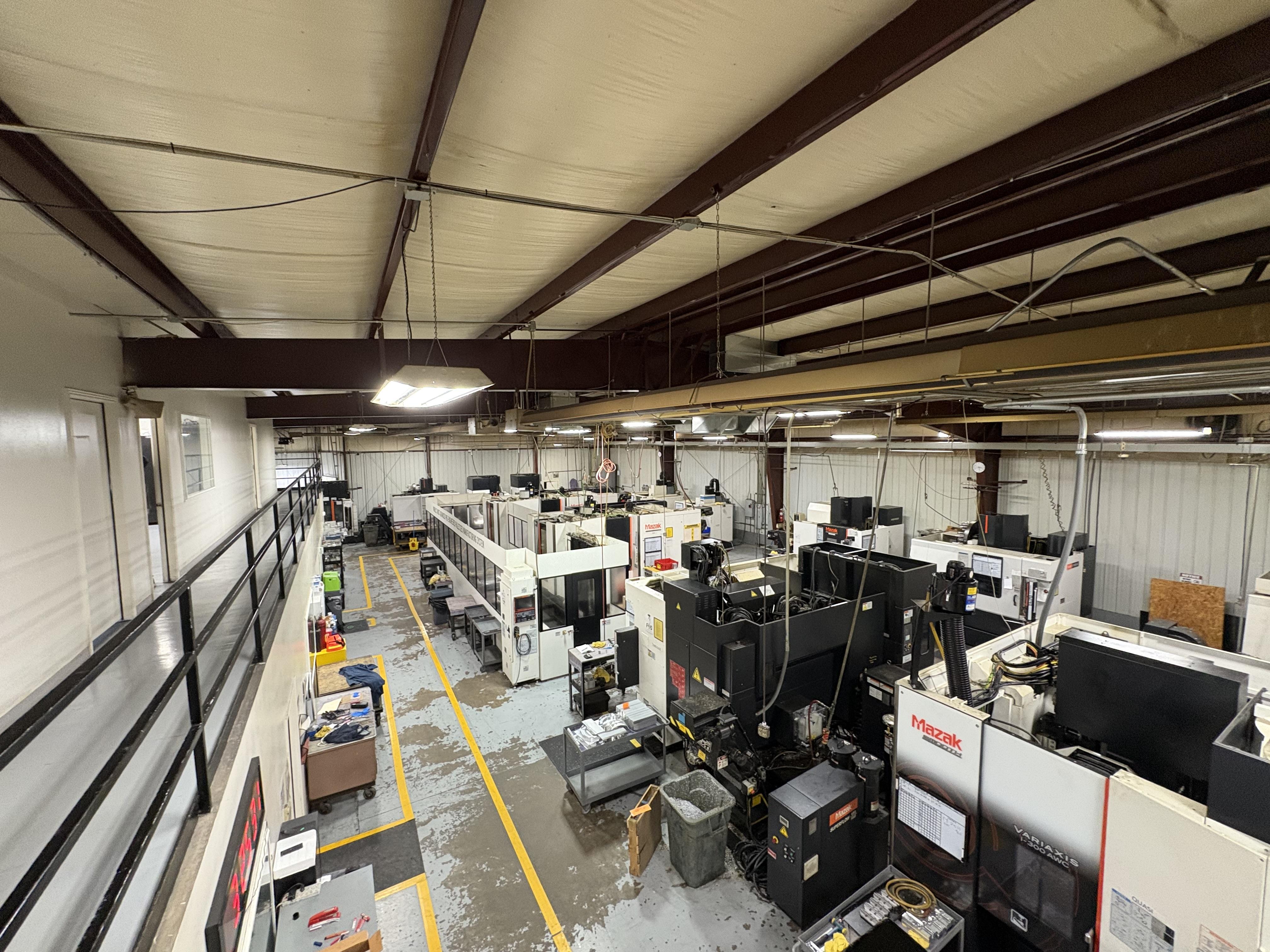 Wide-format building photograph showing east elevation, loading bays, signage area, paved yard, and landscaping.