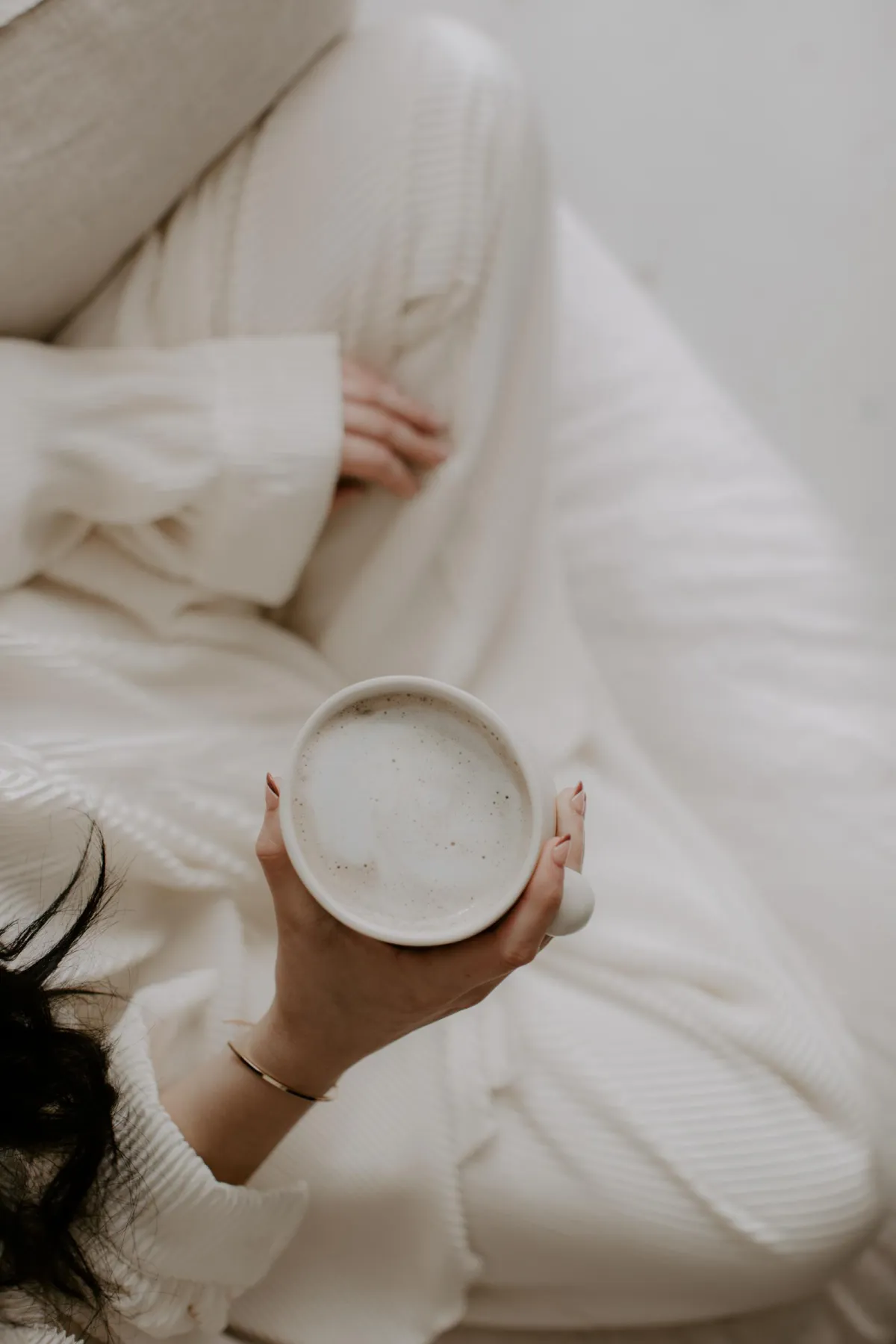 Woman holding warm mug in cozy neutral sweater by sunlit window