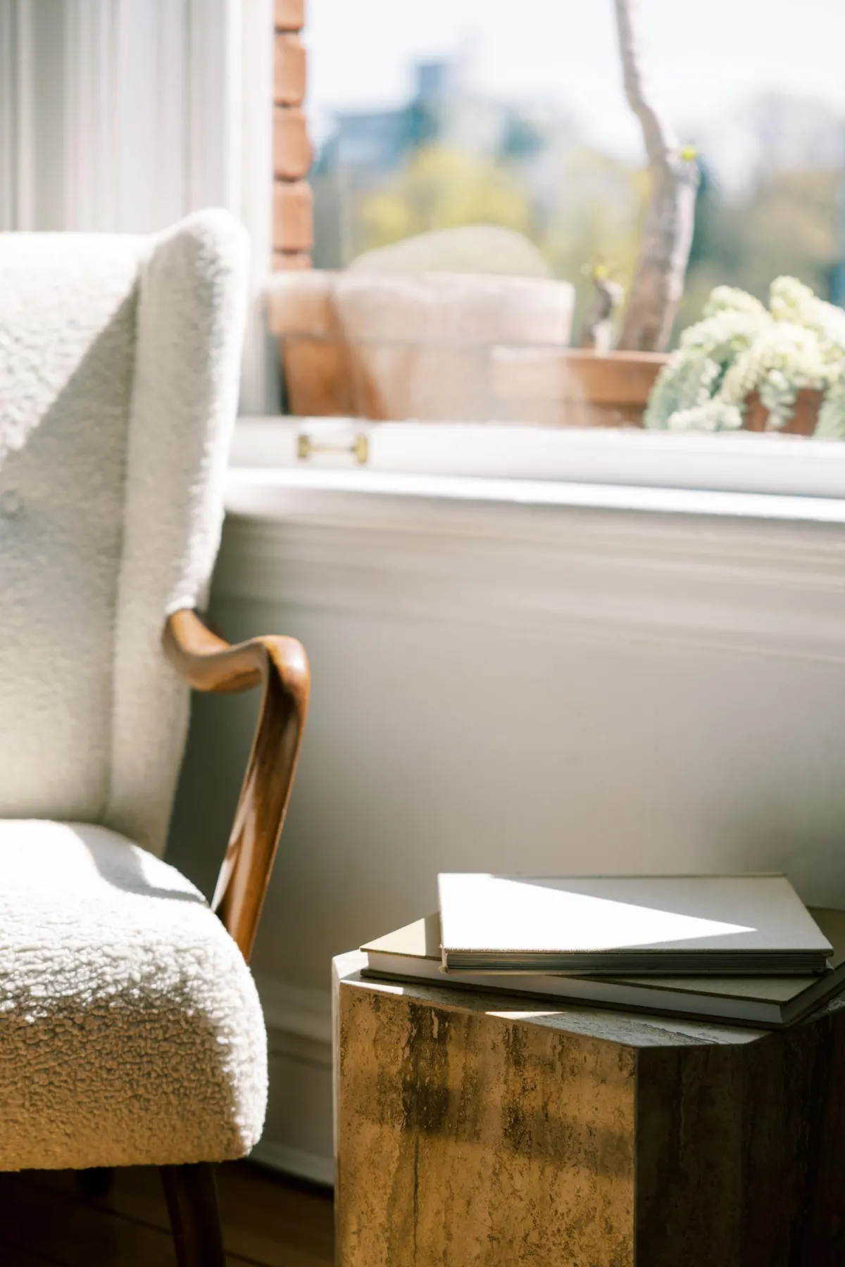 Soft natural light over a cozy reading chair by a window with stacked books and warm neutral textures, creating a calm restorative home corner