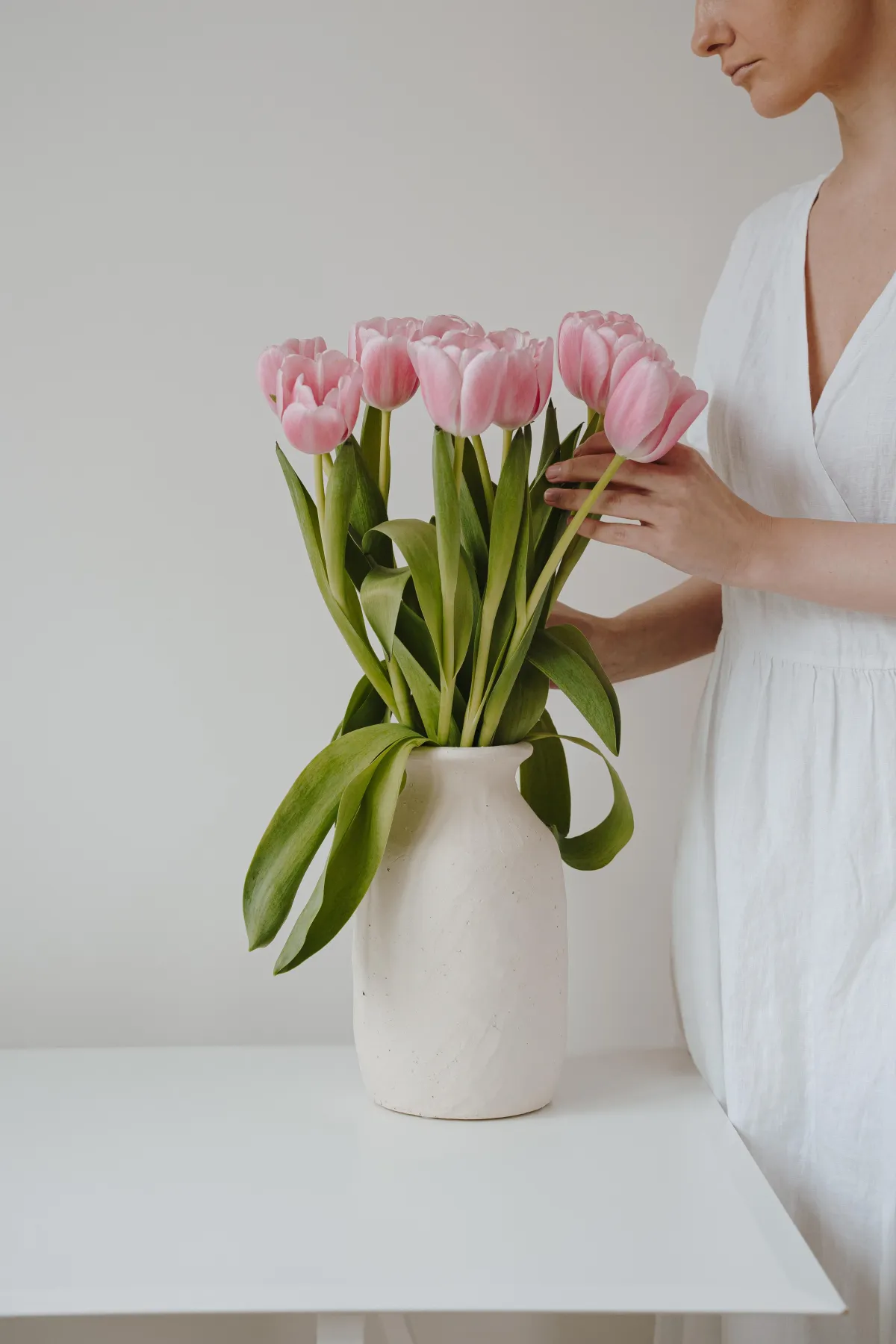 Woman arranging tulips in minimalist ceramic vase, illustrating soft interior styling and gentle home rituals