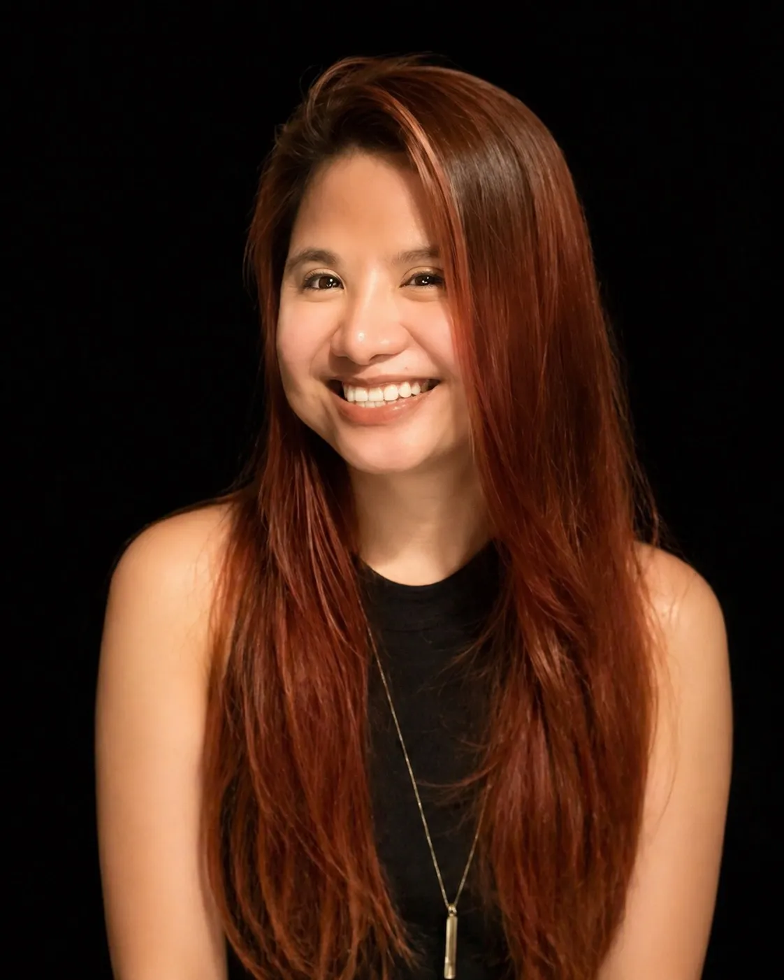 Smiling portrait of Janellyn Briones with copper-red hair, wearing a black top