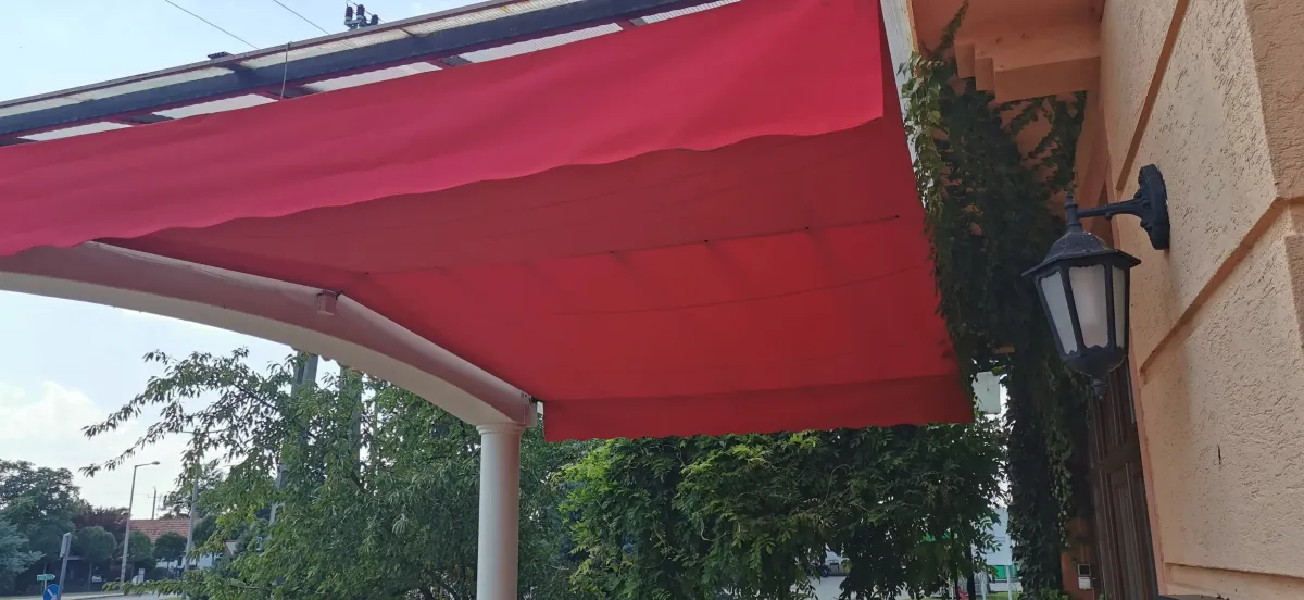 Piros íves napellenző a falra szerelve, klasszikus kültéri lámpa mellett.