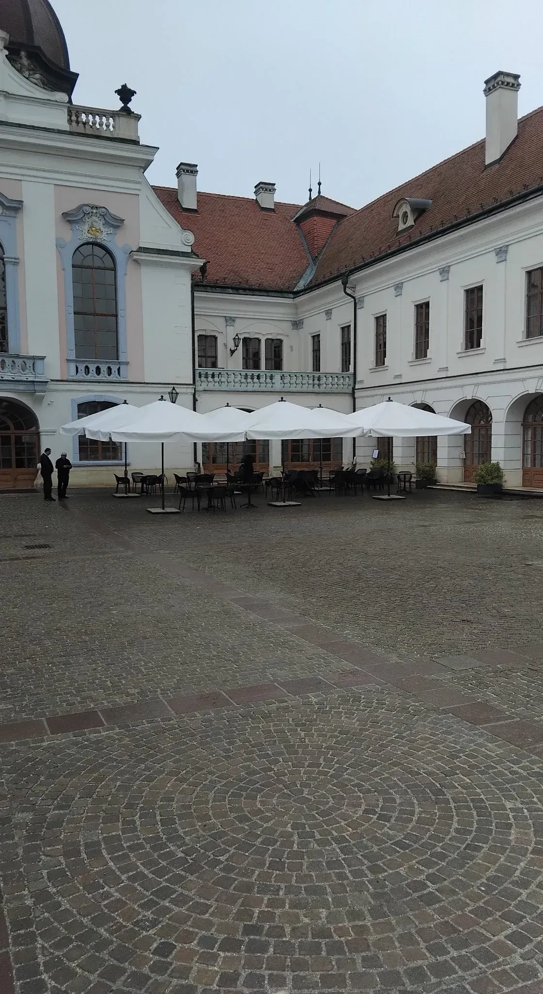 Fehér napernyők egy történelmi kastély udvarán, macskaköves téren elhelyezve.