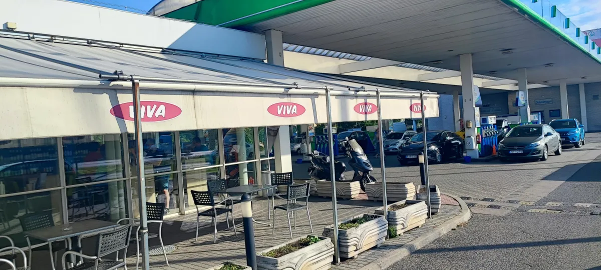 Napernyő talpa kavicsos betétekkel, téglalap alakú burkolaton, körülötte fa és fém székekkel, árnyék vetül a talajra.