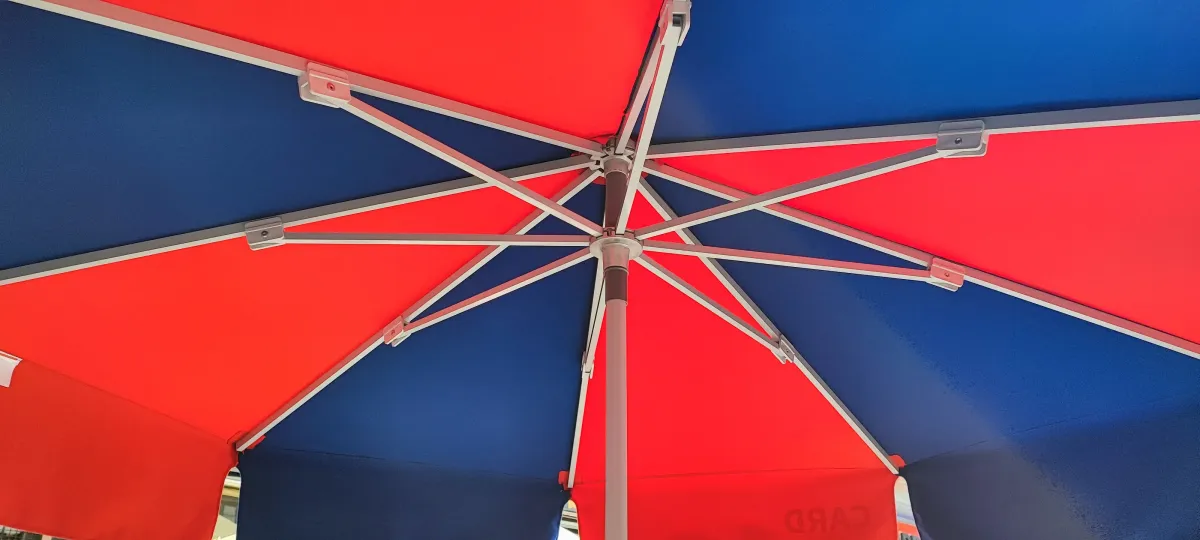 Egy piros és kék színű napernyő belső szerkezete látható alulnézetből. A napernyő fém váza és merevítő rudai szimmetrikusan helyezkednek el, a vászonfelület váltakozva piros és kék háromszögekből áll. Az egész kép a napernyő közepére fókuszál, oldalirányban némi napfény szűrődik be.