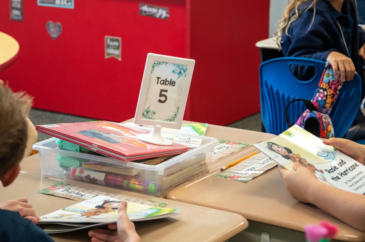 Young readers at a classroom table with stacks of children's books ready for distribution.