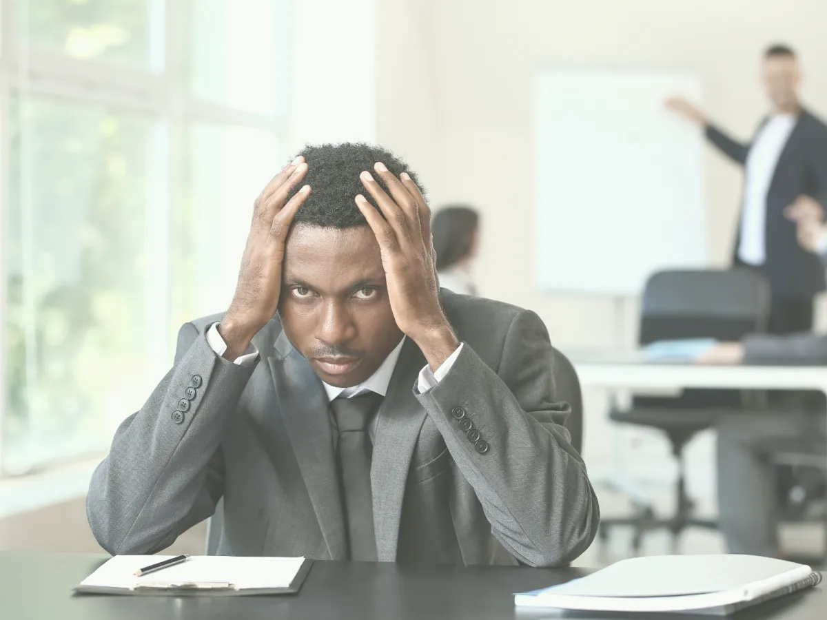 Defeated businessman sitting at desk with head in hands, symbolizing the stress and isolation caused by workplace bullying and a toxic environment.