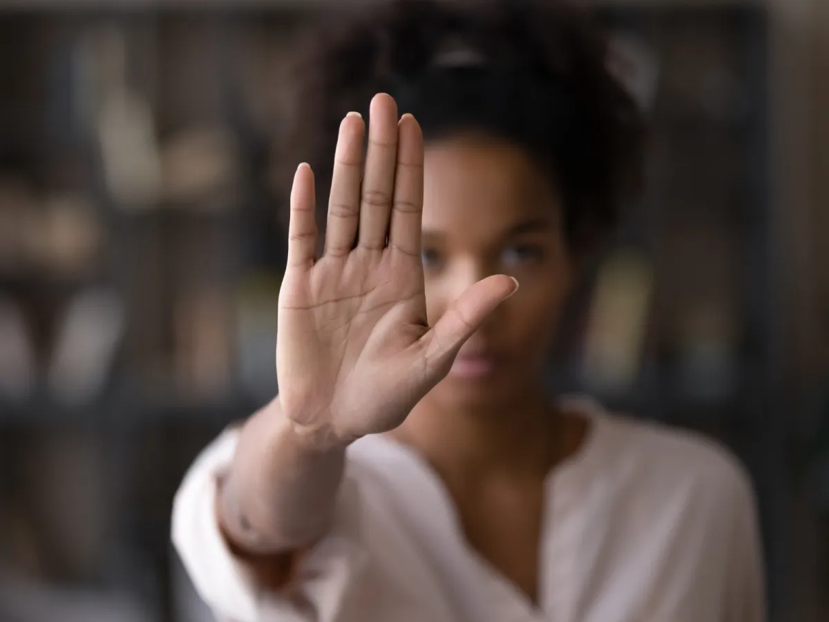 Out-of-focus woman raising her hand in a 'stop' gesture, symbolizing taking action to stop workplace bullying and reclaim control over your career.