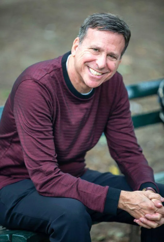 Andy Regal, smiling and seated, embodies resilience and leadership as the host of the Workplace Bullying Summit, sharing his journey and expertise.