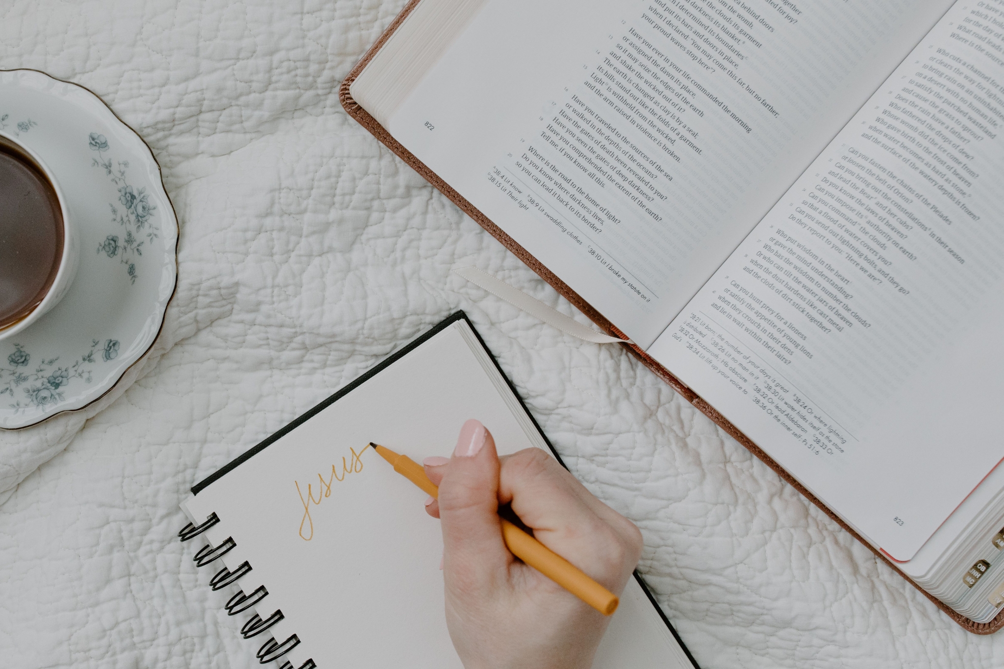 Woman writing in a notebook beside an open Bible and cup of tea