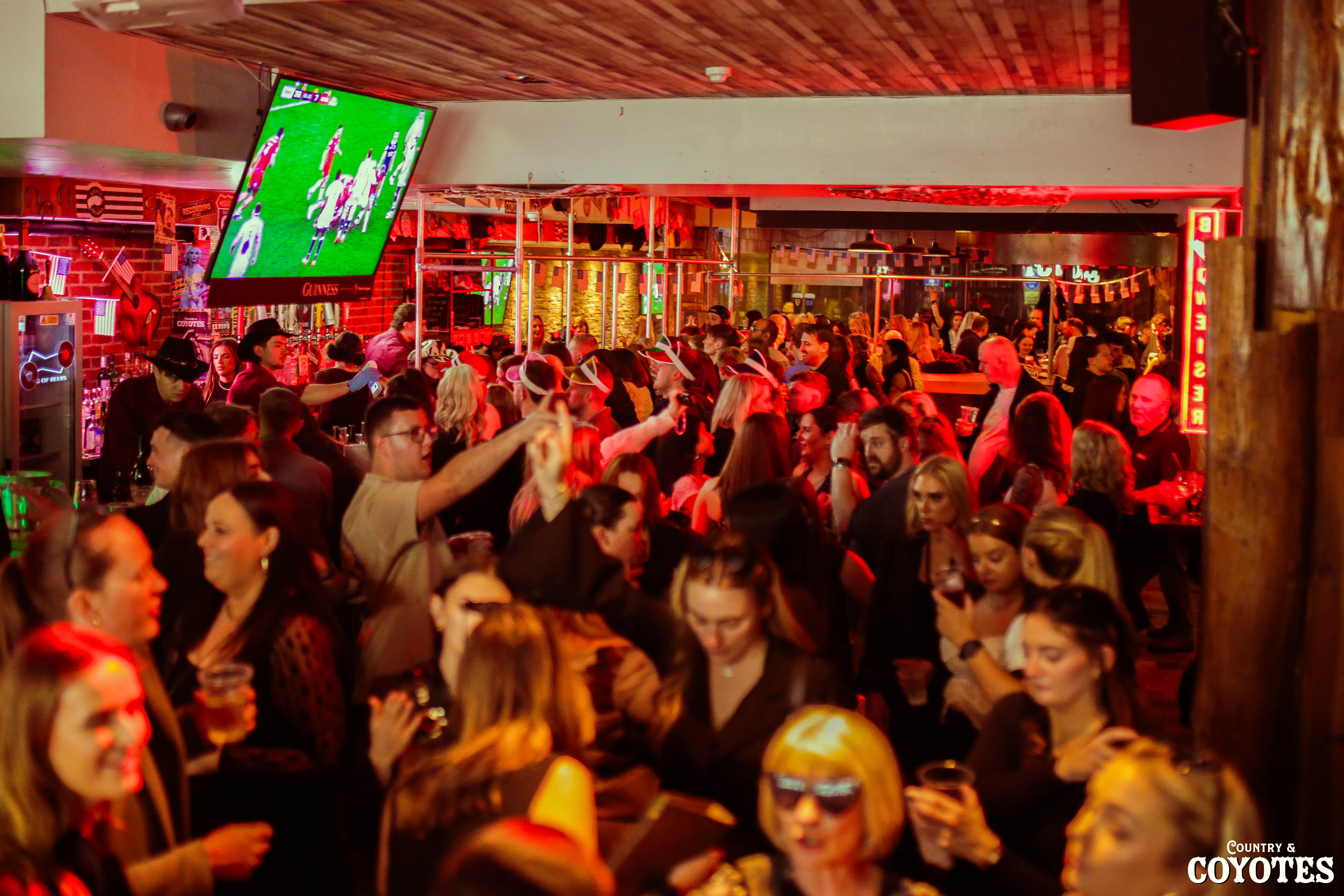 Fans cheering at a packed sports bar with drinks and big screens