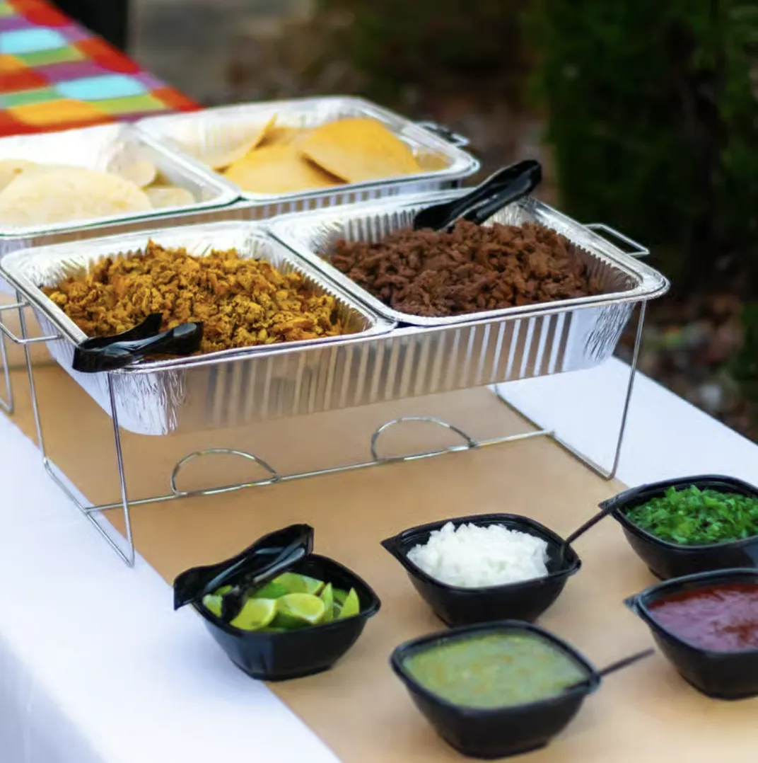 Mexican street food buffet with taco fillings, tortillas, limes, onions, and salsas.