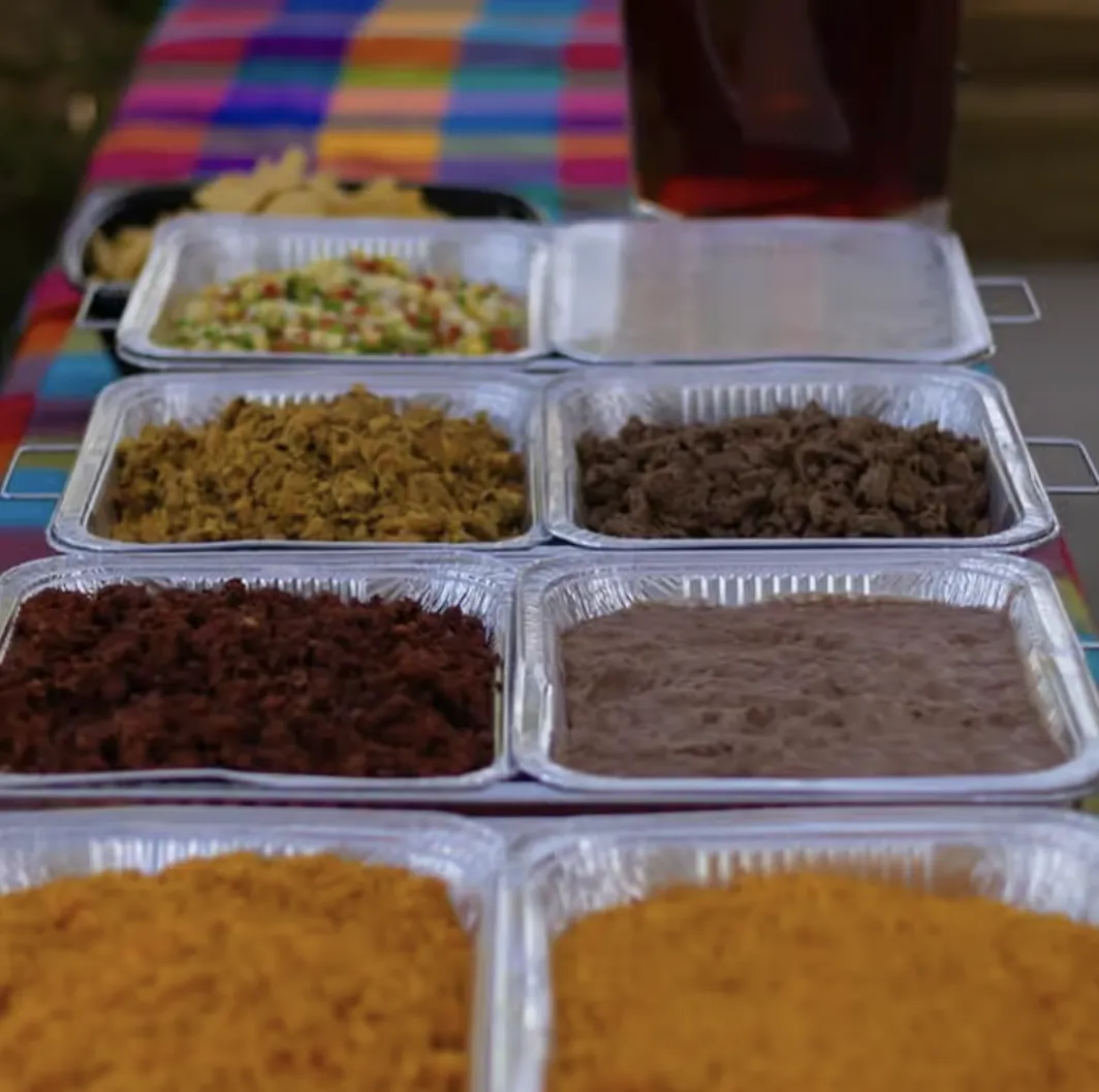 A vibrant spread of Mexican food in foil trays, including rice, beans, and various meats.