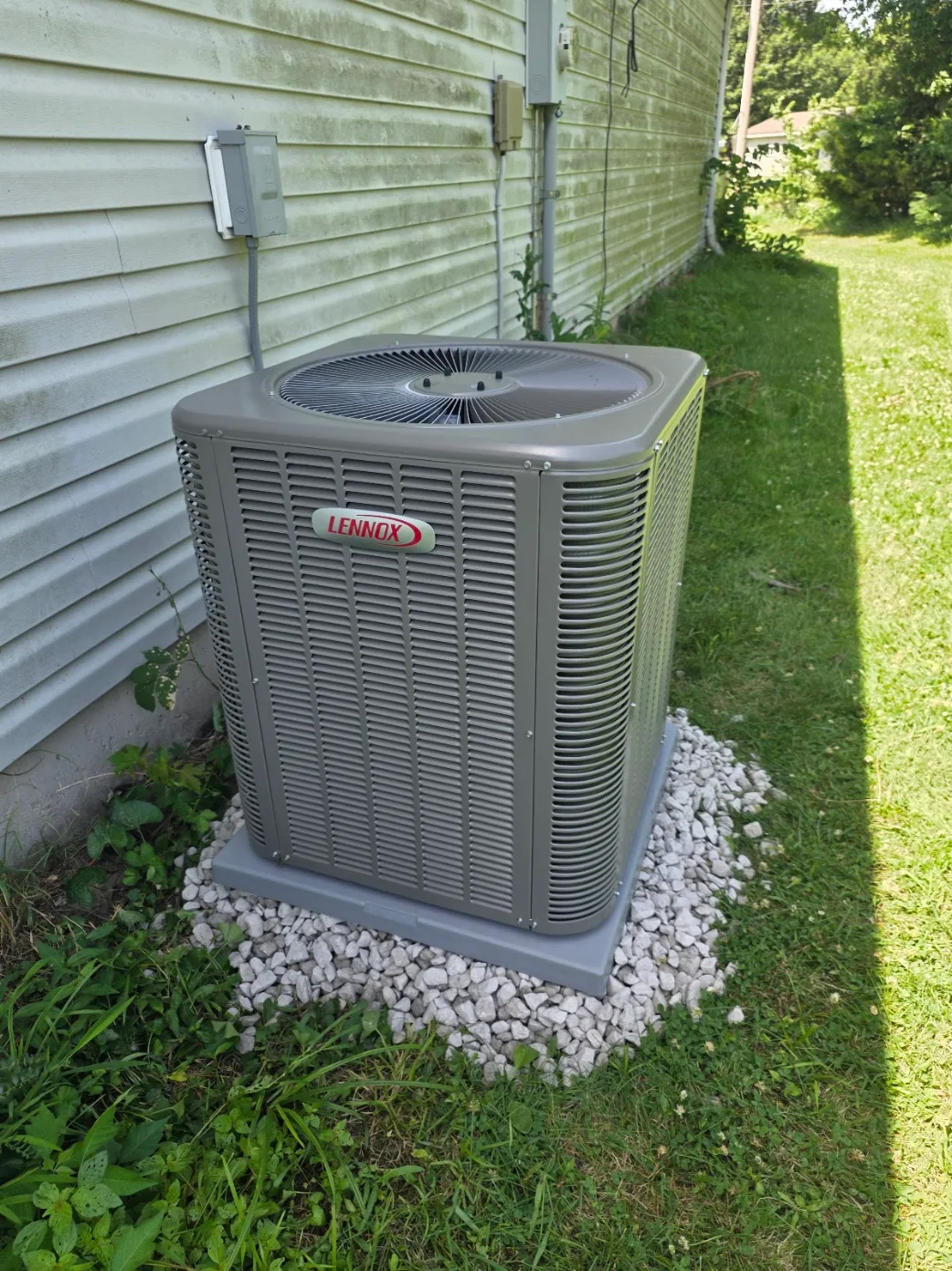 Exterior view of a Lennox AC condenser unit properly installed next to wood siding in an Overland Park, KS backyard with clean refrigerant lines.