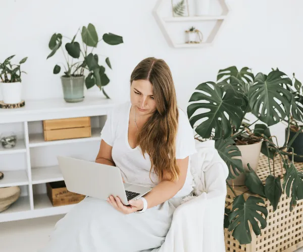A professional working intentionally on a laptop computer in a bright, clean, peaceful home office space filled with indoor plants.