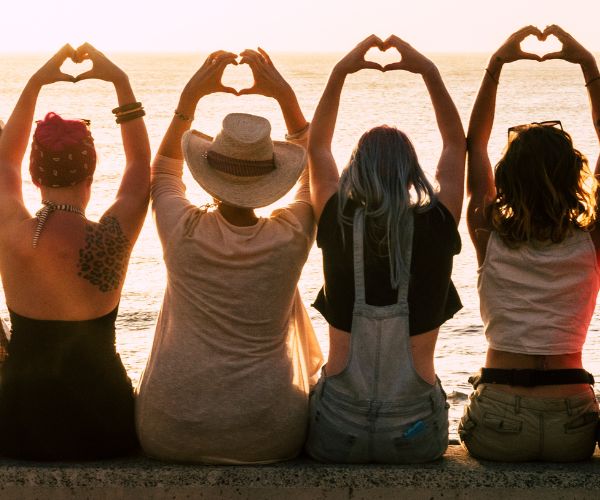A group of women sitting comfortably in a supportive circle on yoga mats and floor cushions in a brightly lit, tranquil wellness studio.