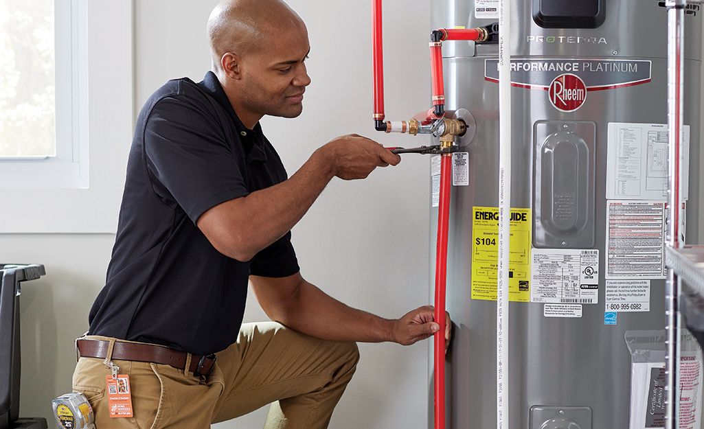 Professional plumber repairing a residential water heater in a utility room, tightening pipe connections with tools for Lion Plumbing water heater repair services.