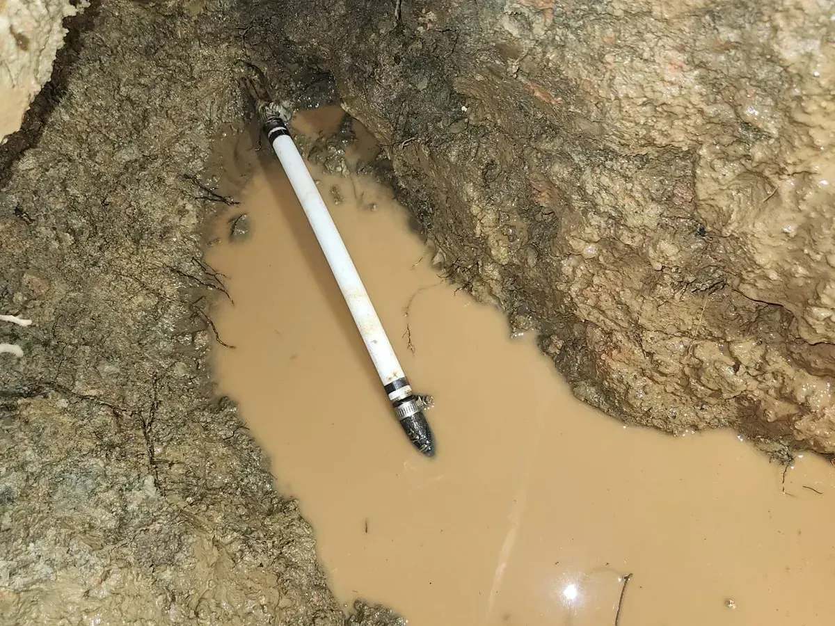 Broken underground PVC pipe exposed in muddy hole filled with standing brown water