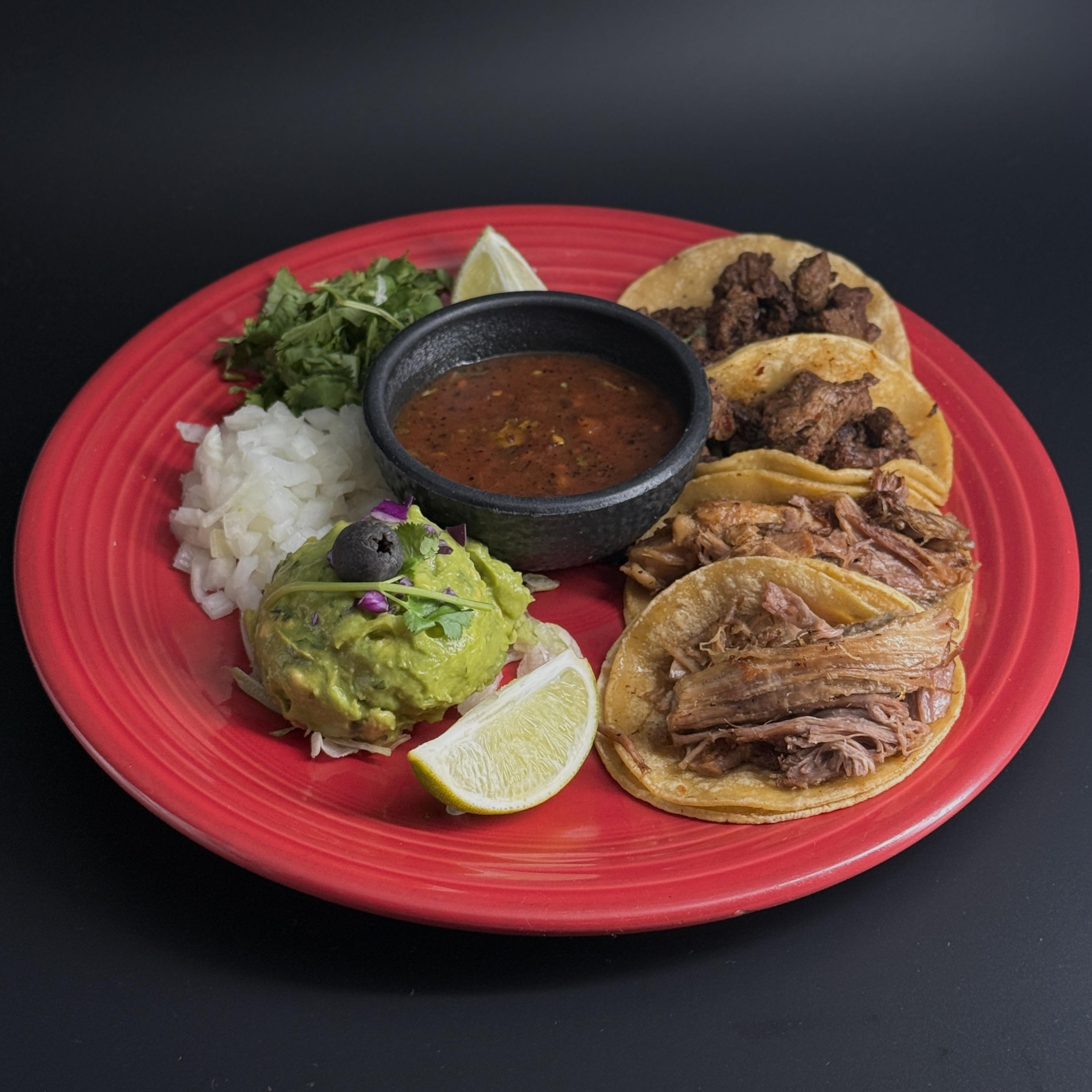 Taco Sampler: Four soft corn tacos, two carne asada and two carnitas, topped with fresh onion, cilantro, queso cotija, guacamole and salsa quemada.