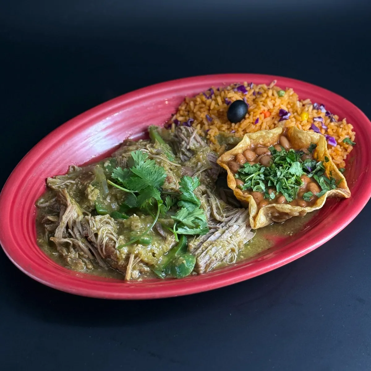 Chile Verde - Pork carnitas sautéed in a tangy tomatillo sauce with onions and green peppers. Served with arroz Mexicano and homestyle frijoles de la olla, accompanied by warm tortillas.