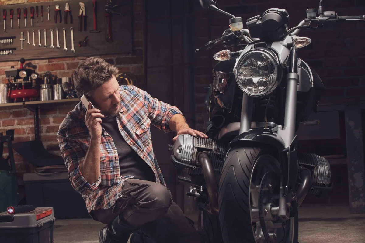 Man leaning next to a motorcycle making a call