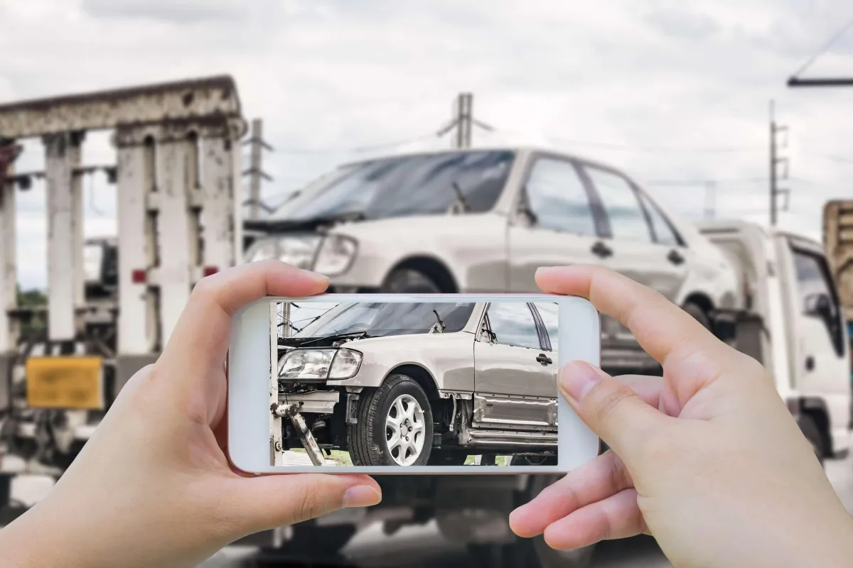 pair of hands holding phone taking picture of a car on a flatbed of a tow truck