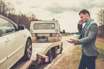 Man making a call while car is being loaded on a tow truck