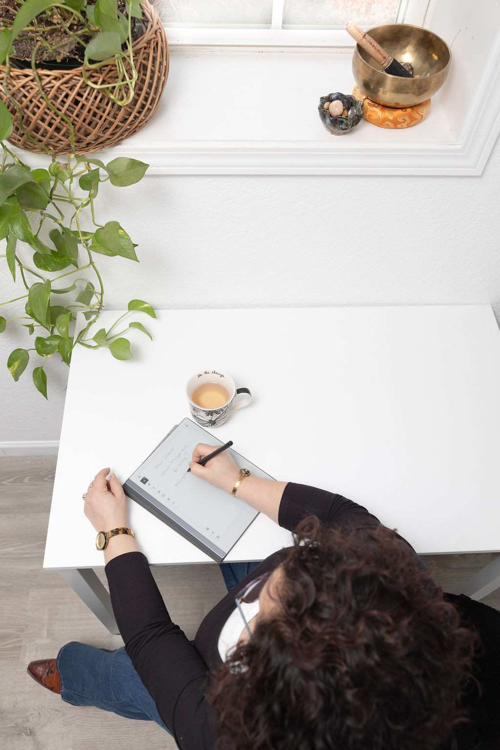 Tracie Merwitzer writing session notes at her desk with a singing bowl, tea, and plants in her Asheville hypnotherapy practice.