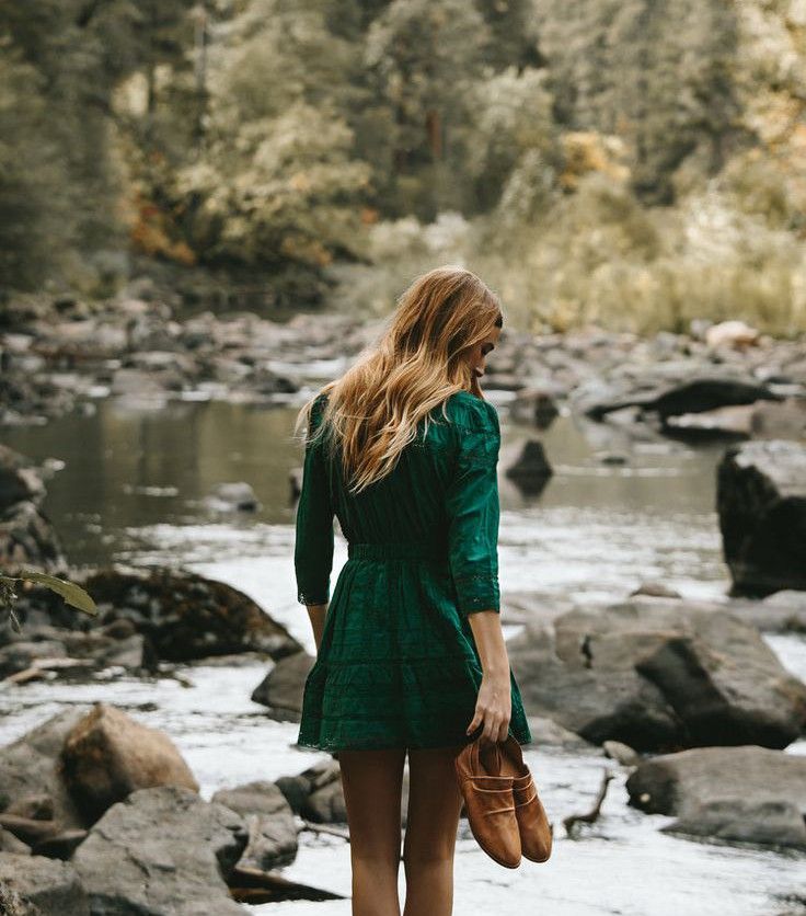 Woman standing reflectively by a forest creek, representing the pause and self-discovery that life coaching and hypnotherapy support.