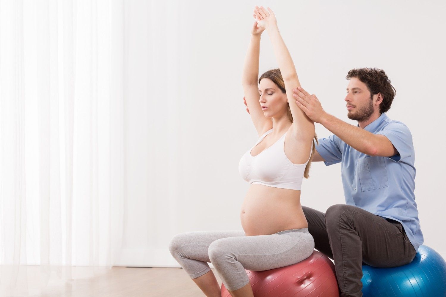 Pregnant woman stretching on a birthing ball with her partner's support during hypnobirthing preparation for a calm, confident birth.