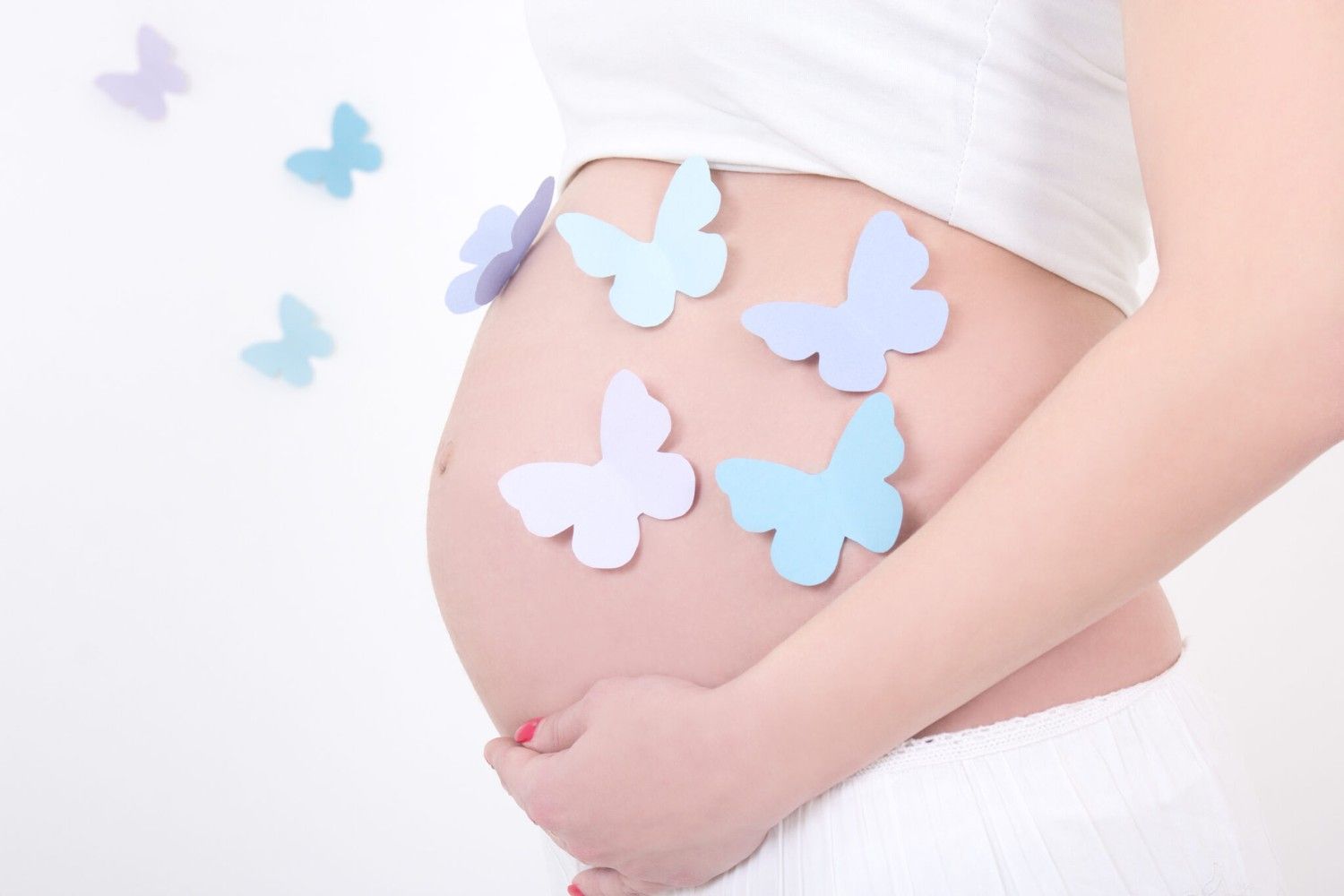 Pregnant woman cradling her belly with soft pastel paper butterflies, representing gentle fertility support and hypnobirthing preparation at The Butterfly Effect.