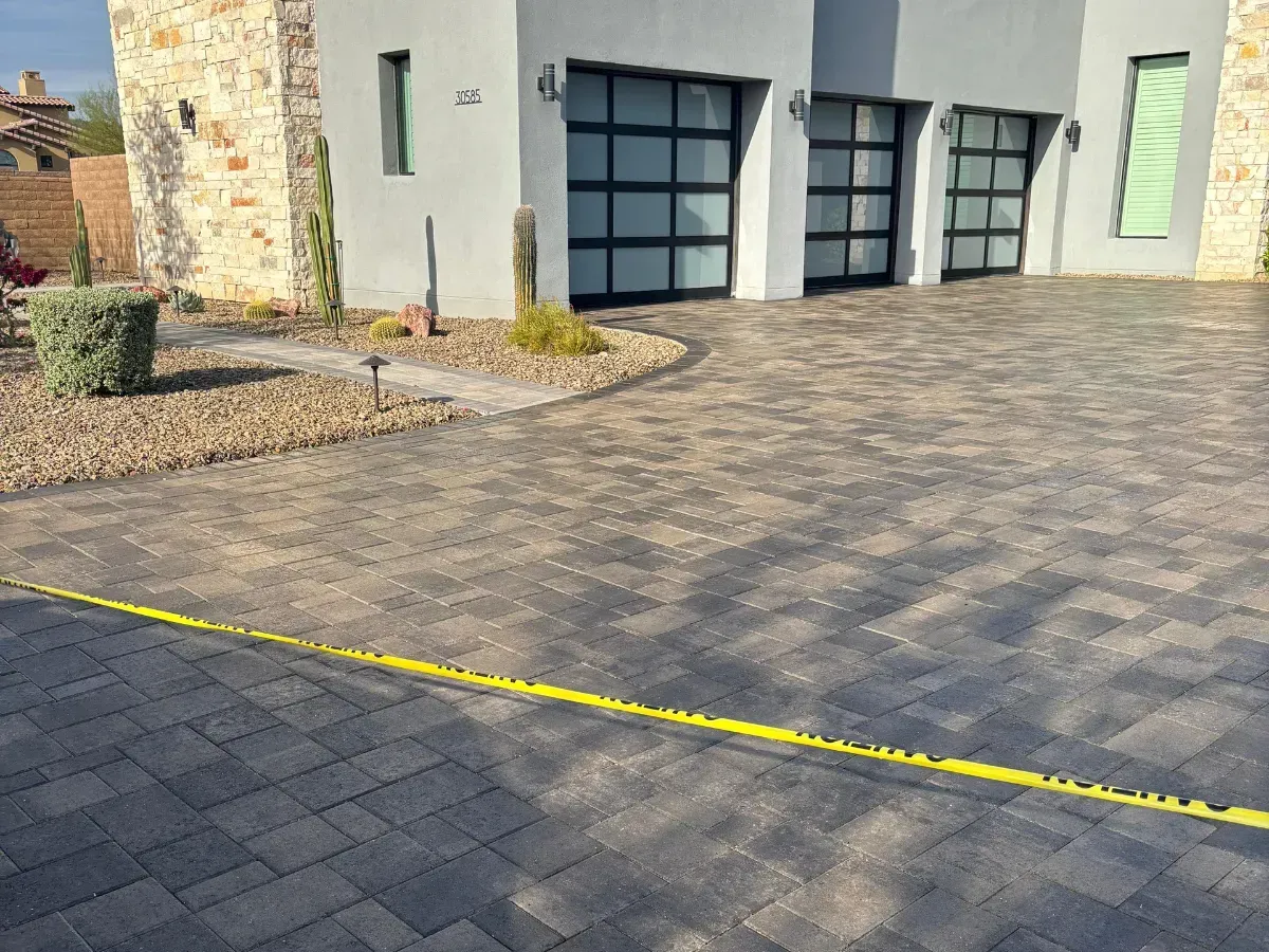 A modern house with a paver driveway, desert landscaping, and yellow caution tape across the foreground.
