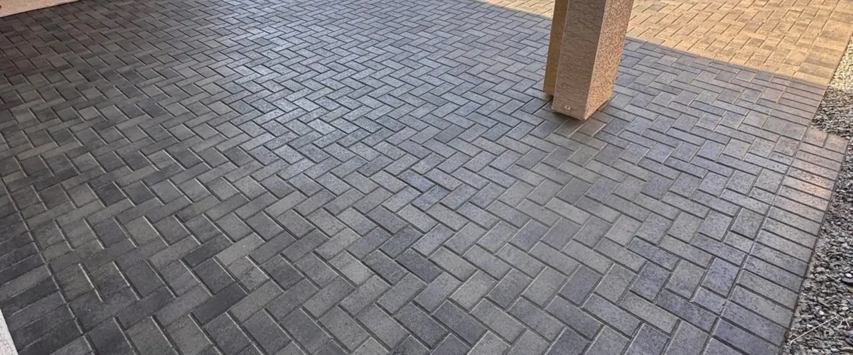 Clean herringbone pattern paver patio with dark brick pavers and a stone pillar, showcasing a freshly cleaned outdoor paved surface.