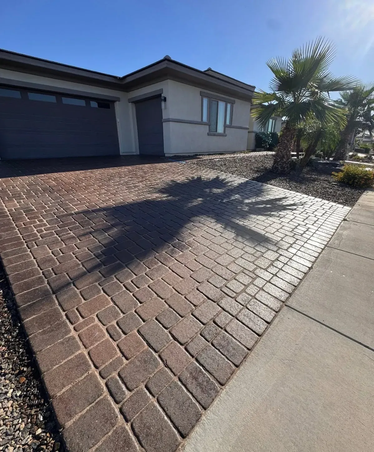 Residential driveway with cleaned brick pavers, palm tree shadows, and a well-maintained paved walkway leading to a modern home.
