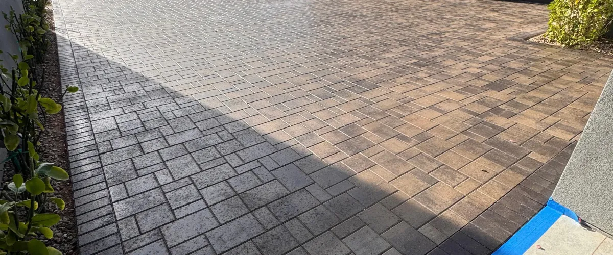 A paver driveway showing a clear line between a dirty, uncleaned left side and a clean, power-washed right side.