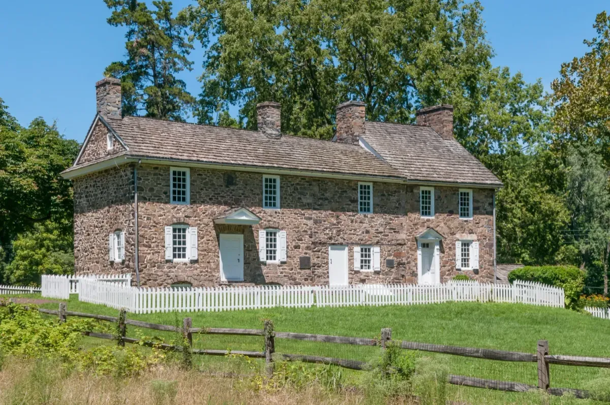 Historic stone house with a white picket fence and a green lawn