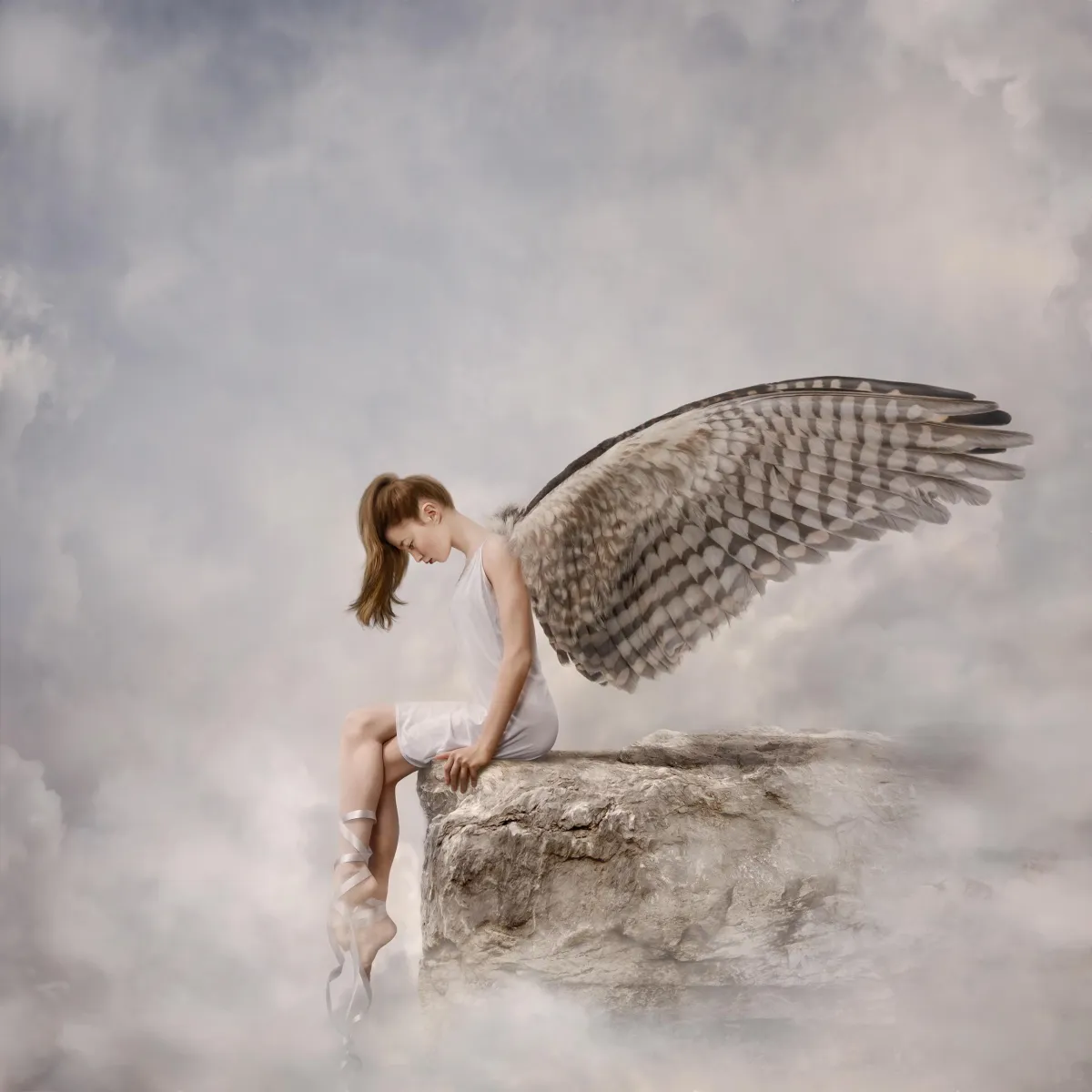 A photography composite image by Alana Lee of a girl dancer with wings sitting on the edge of a cliff in the clouds