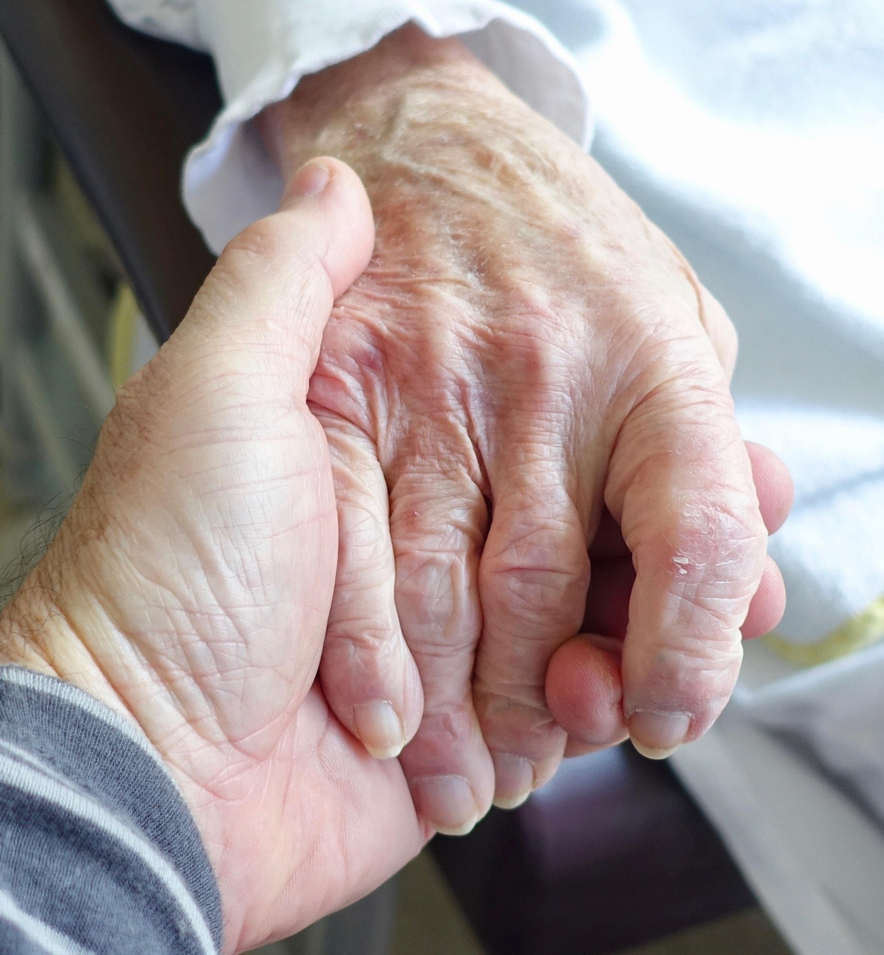 Close-up of caregiver and senior holding hands, representing dignity and connection.