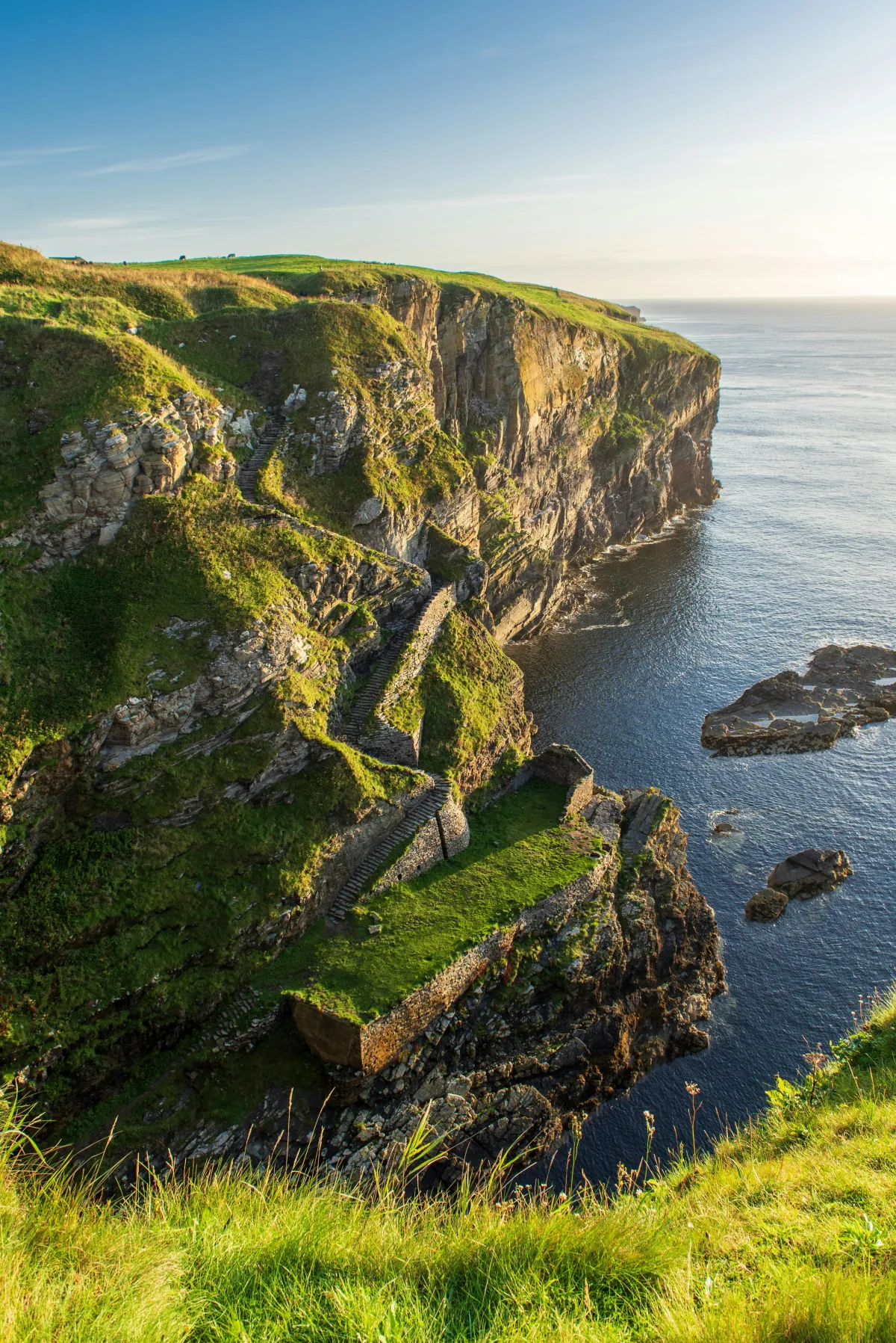 Dramatic coastal cliffs with ancient stone steps winding down the green hillside to the ocean, representing the structured learning path and natural progression students follow through TCLi Academy's curriculum