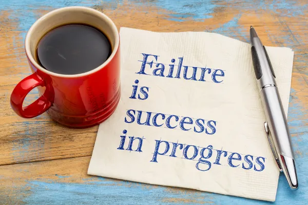 Cup of coffee with note on napkin that says Failure is success in progresss