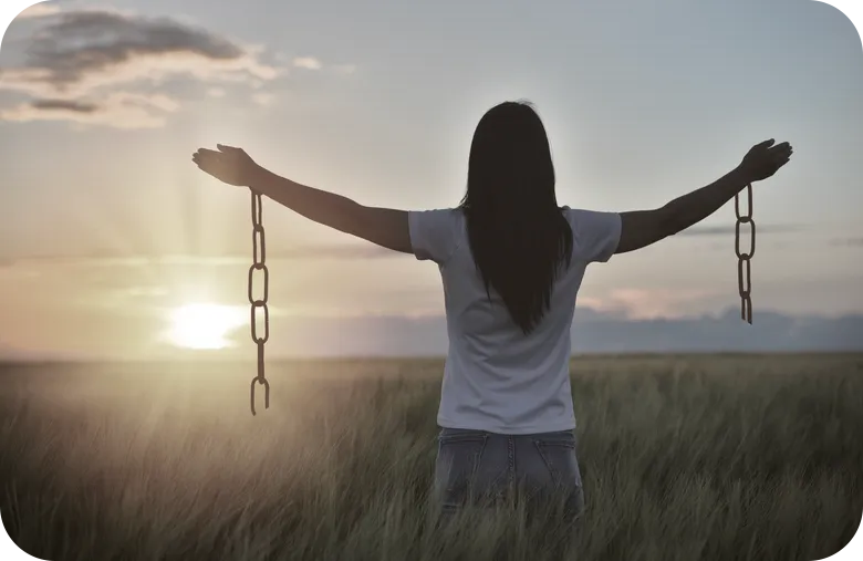 woman with arms aised and chains broken from her wrists looking at sunset