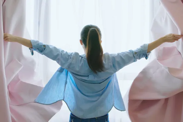 Confident woman throwing open the curtains in morning light.