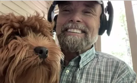 Smiling man with headphones holding a dog, sharing positive testimonial experience