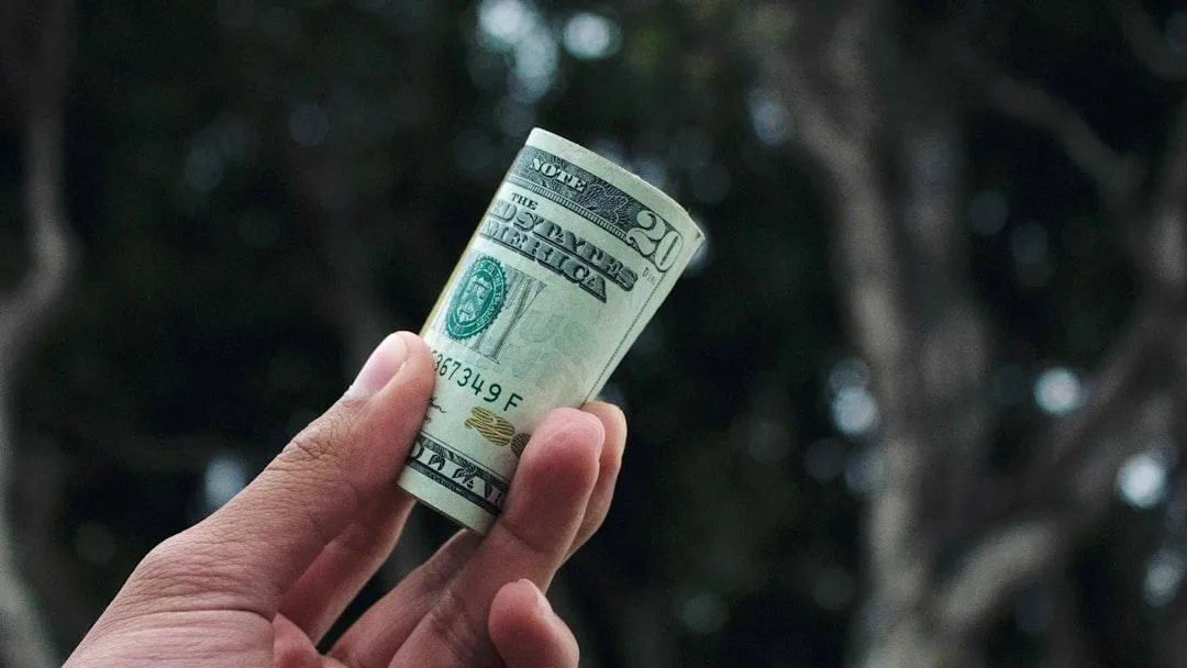 Hand holding a rolled-up dollar bill symbolizing recurring income and financial growth.