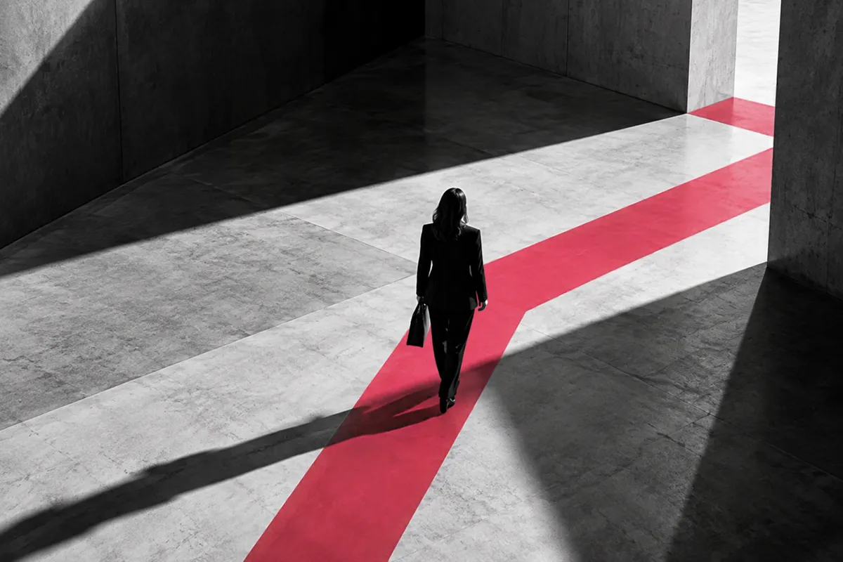 Mujer de negocios caminando sobre una ruta roja en un entorno arquitectónico en blanco y negro, símbolo de claridad, dirección estratégica y toma de decisiones empresariales.