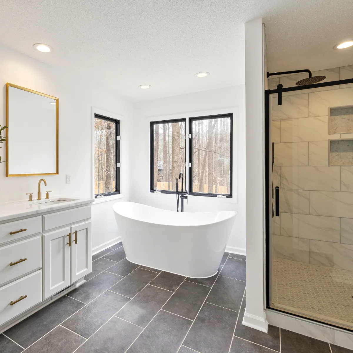 Modern bathroom remodel with freestanding soaking tub glass shower and white vanity featuring gold fixtures